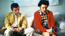 a young man in a yellow jacket and a young woman in a red jacket sit next to each other on the couch